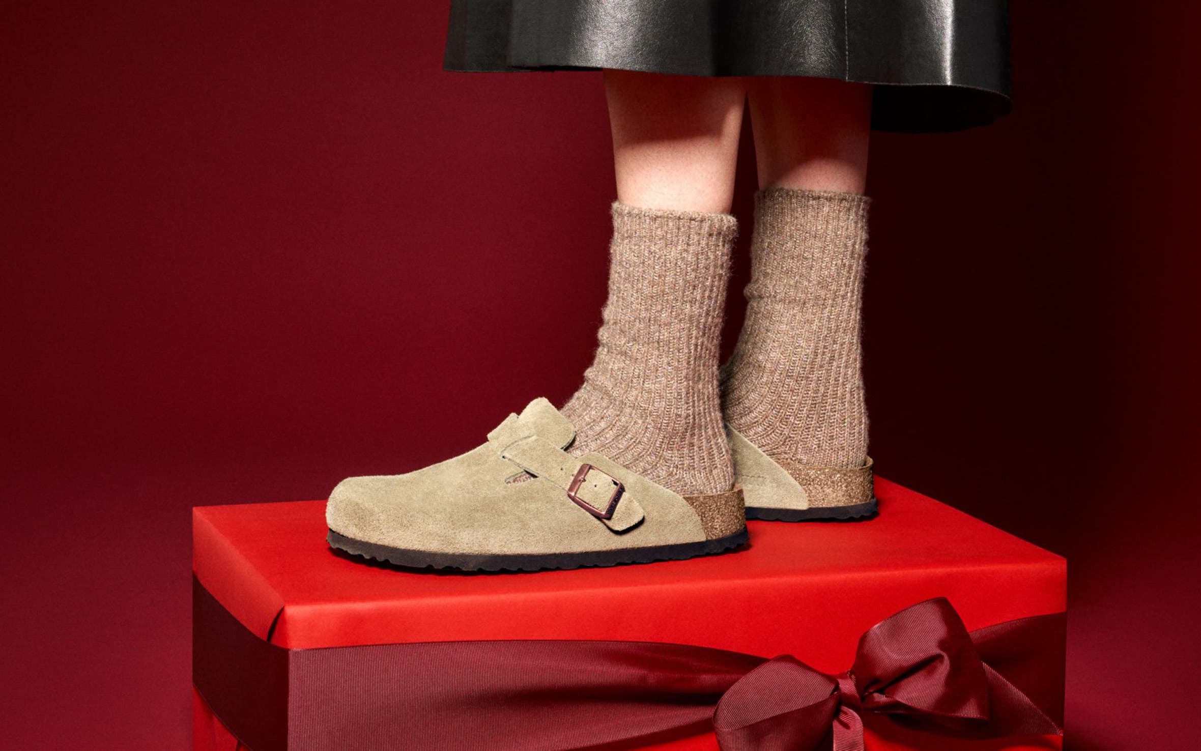 A person wearing Birkenstock clogs standing on a red gift box