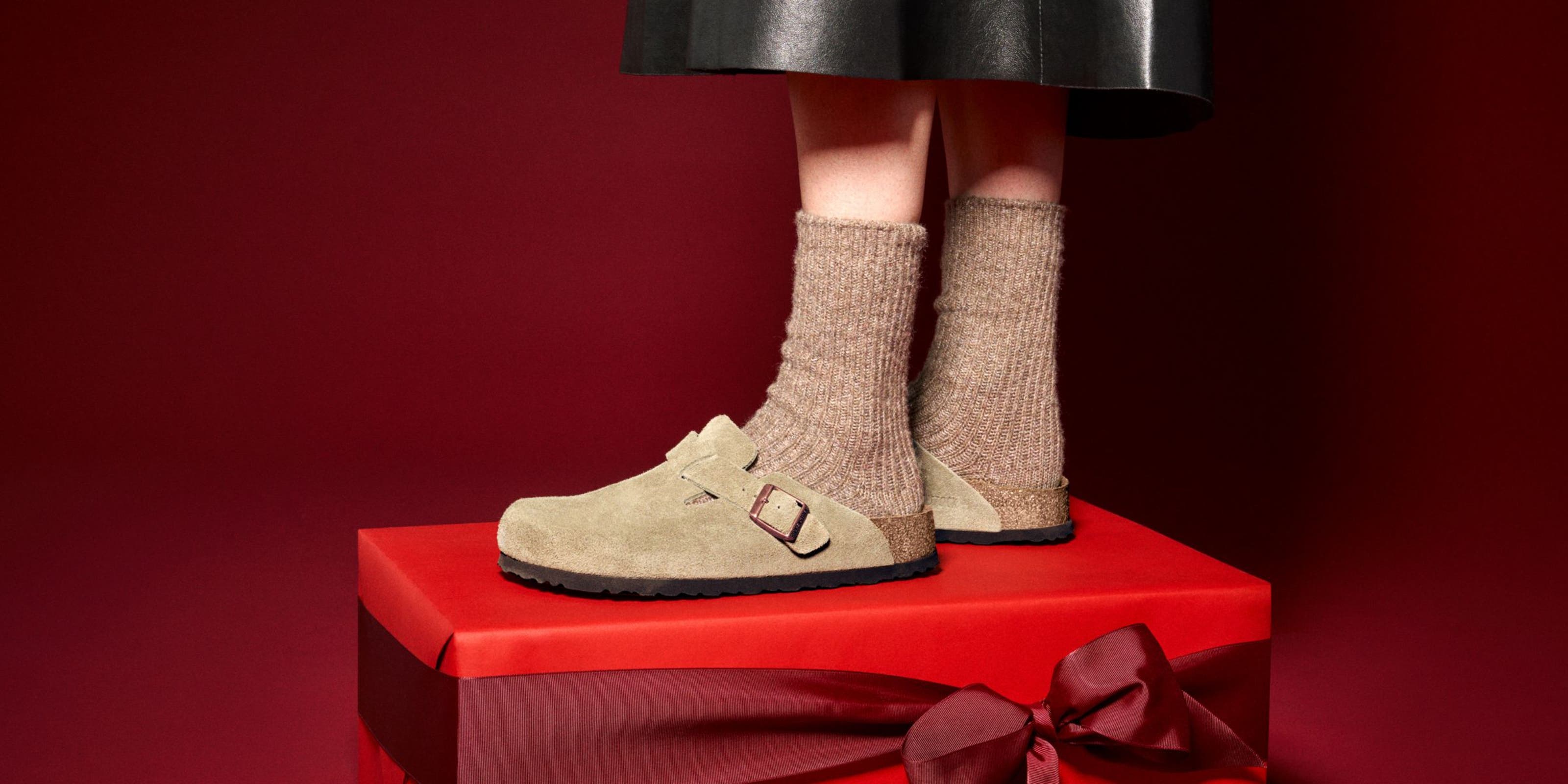 A person wearing Birkenstock clogs standing on a red gift box