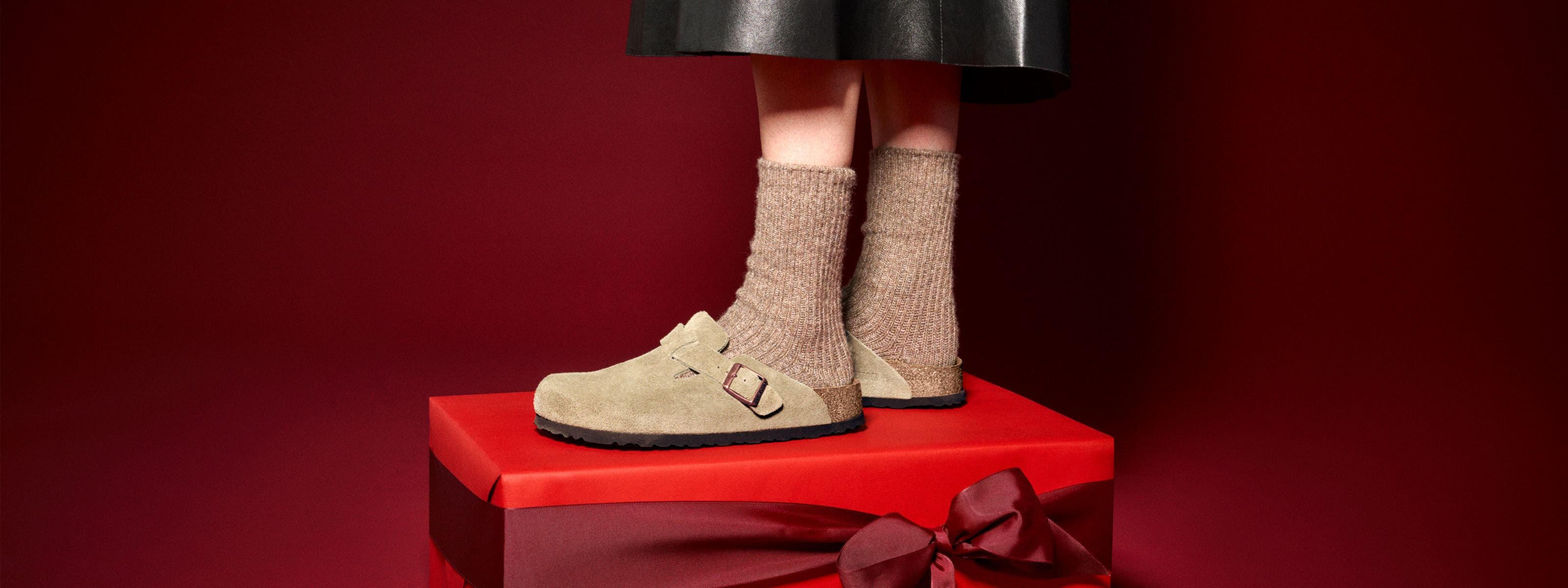 A person wearing Birkenstock clogs standing on a red gift box