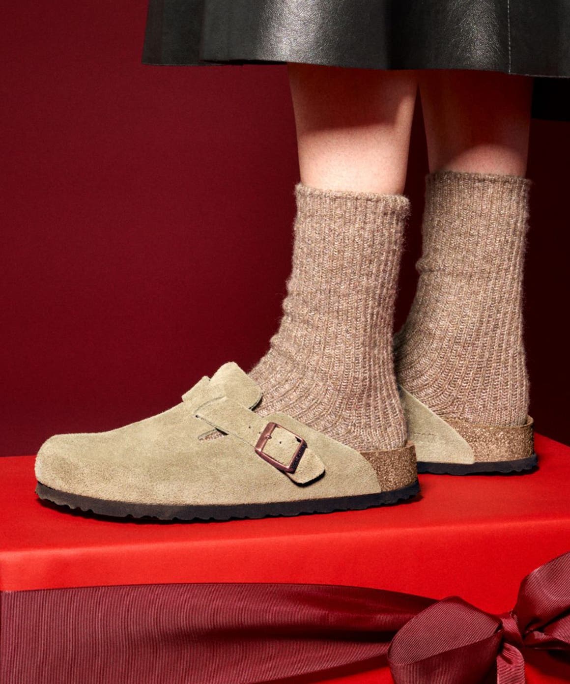 A person wearing Birkenstock clogs standing on a red gift box