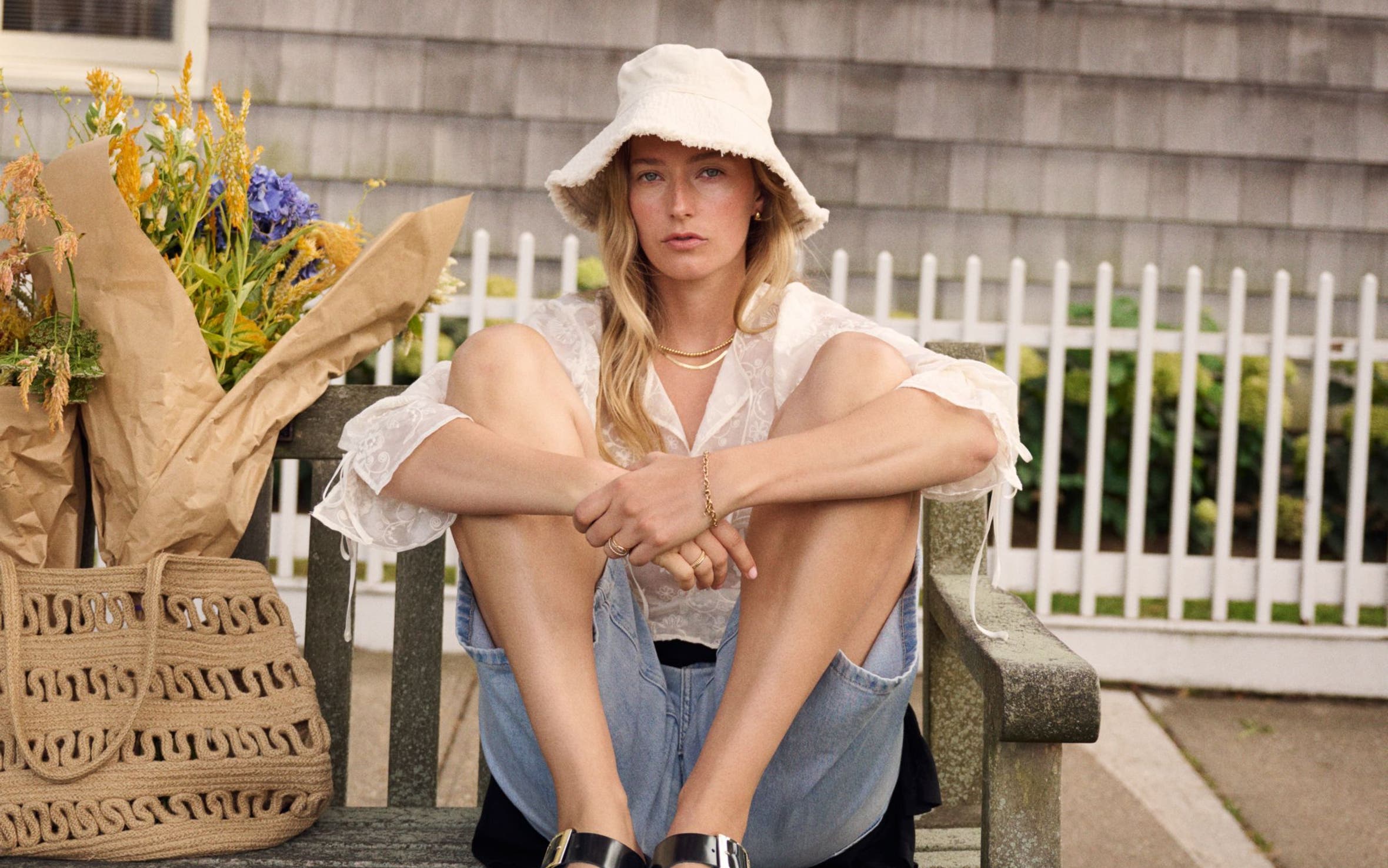 A woman on a weathered bench in light denim jeans, a white sun hat and black leather Birkenstocks sandals.