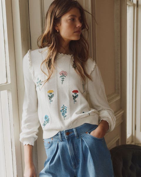Women wearing white pullover sweater with embroidered flowers.