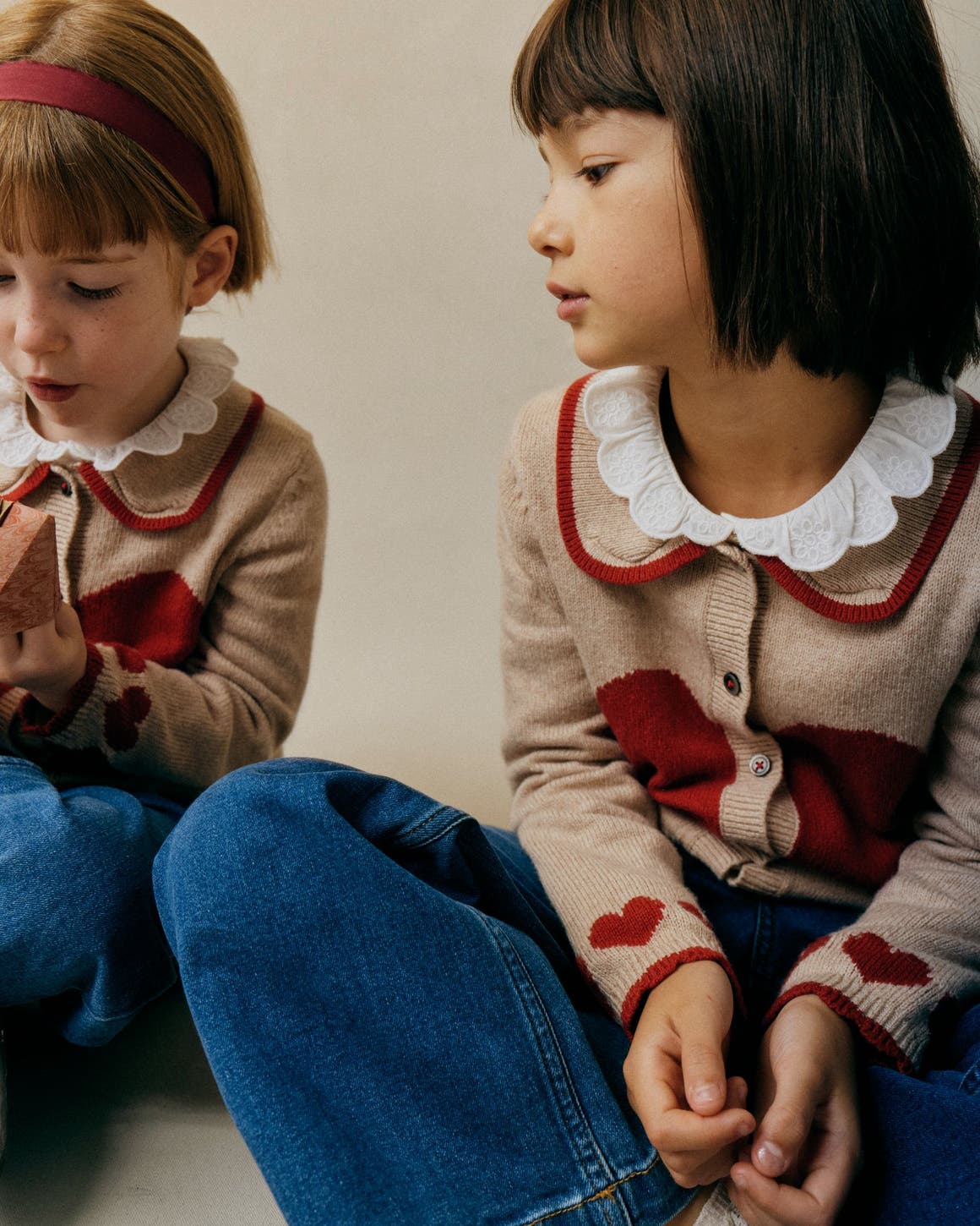 Two little girls wearing matching Mini Boden heart cardigans.