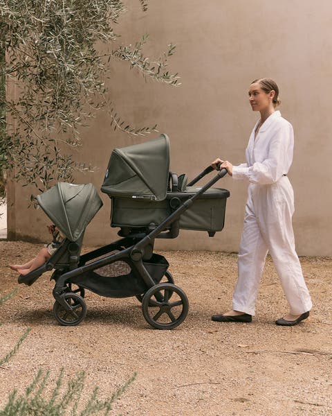 Woman pushing an olive green double stroller.