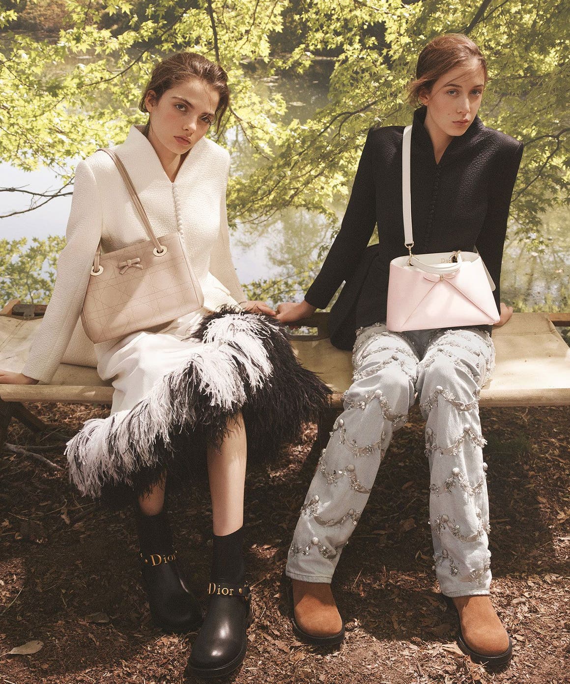 Two women seated outdoors on a wooden bench, wearing Dior tailoring and accessories in a wooded, waterside setting