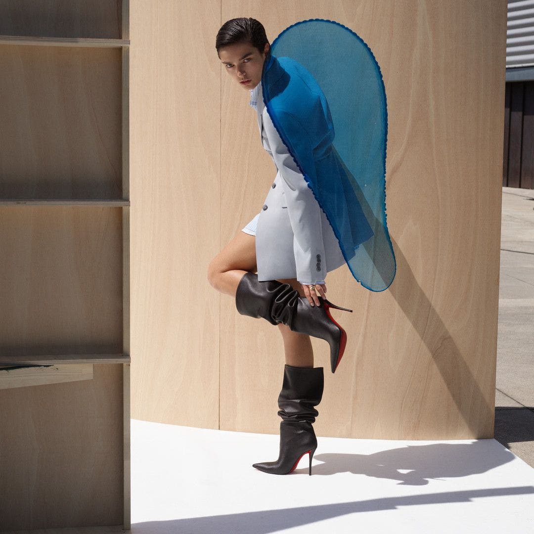 Woman wearing slouchy black leather boots with a pointed toe and red sole by Christian Louboutin.