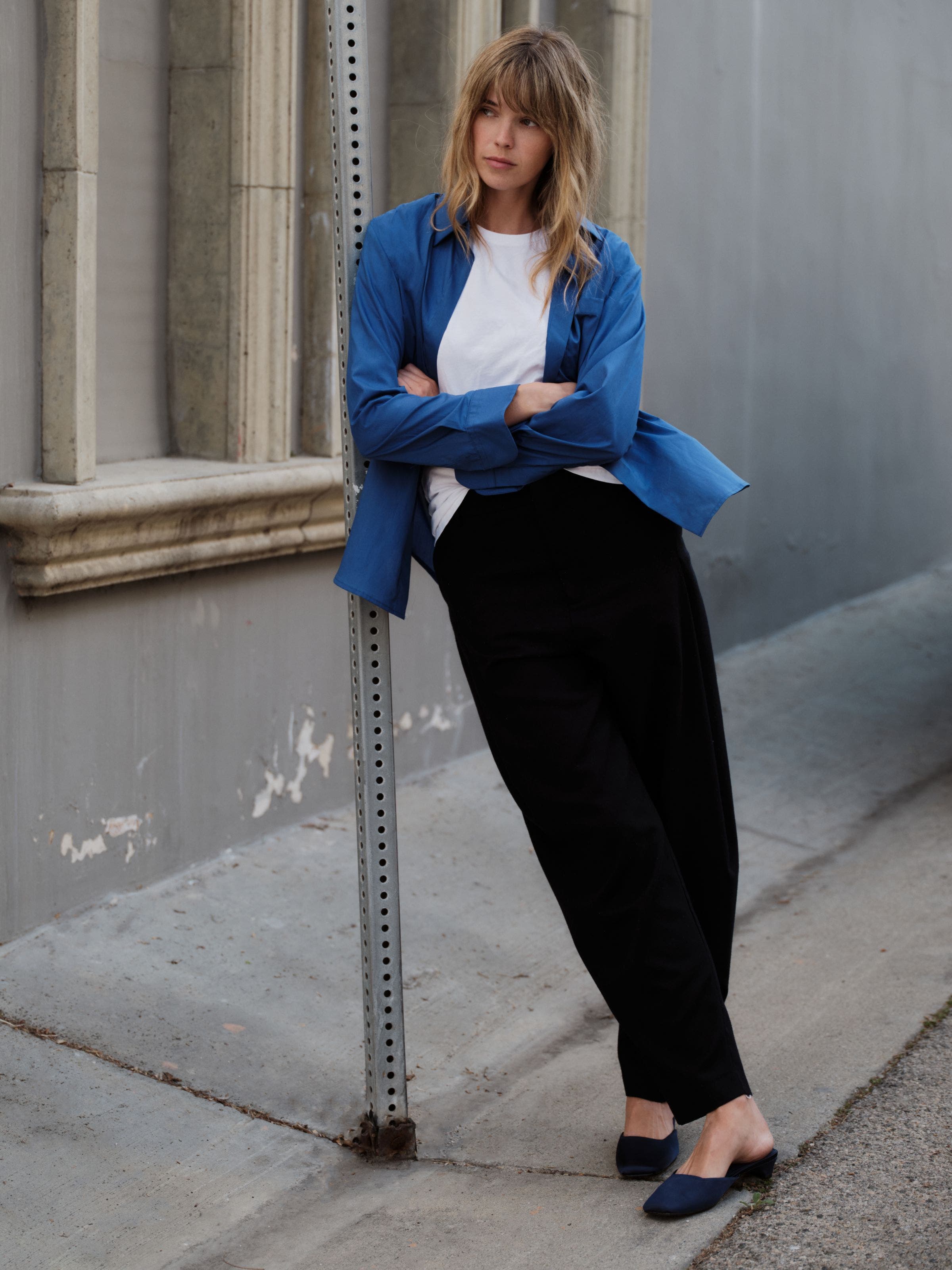 A woman wearing a white t-shirt, a blue button up, and black trousers.