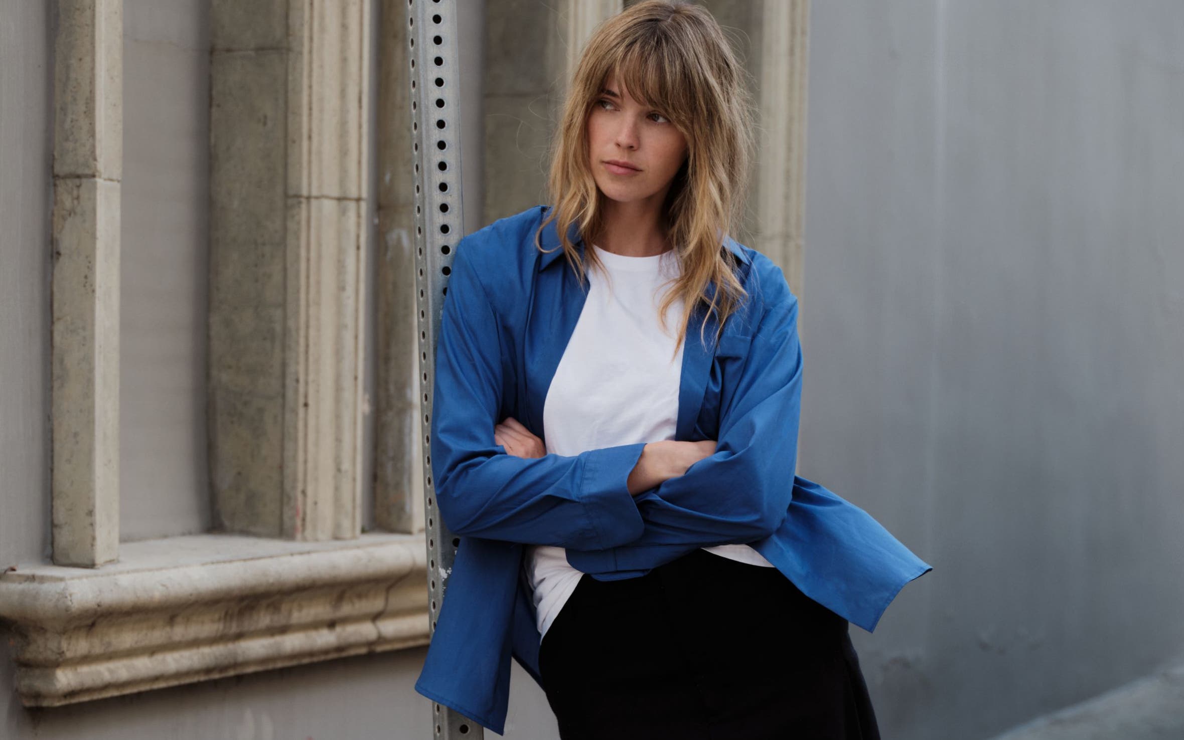 A woman wearing a white t-shirt, a blue button up, and black trousers.