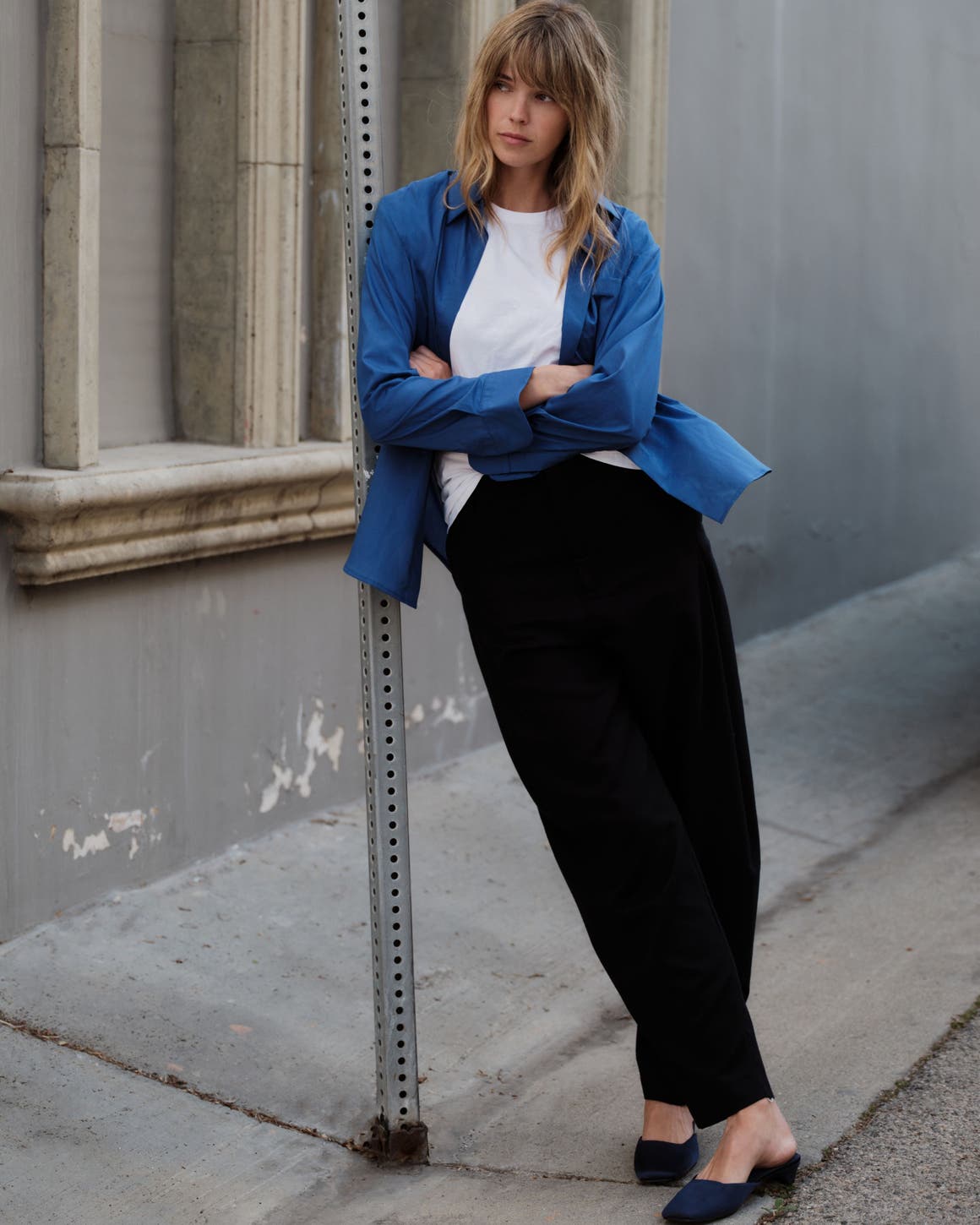 A woman wearing a white t-shirt, a blue button up, and black trousers.