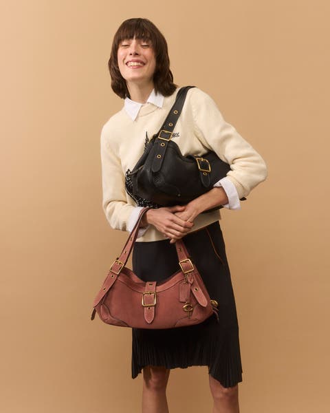 A woman wearing a sweater and skirt holding two buckle handbags.