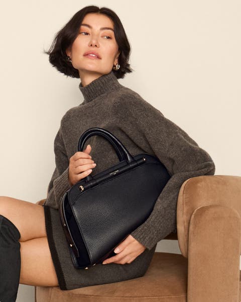 Woman sitting on a chair holding a black handbag from Cole Haan