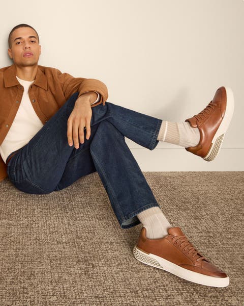 Man wearing brown jacket, jeans and pair of Cole Haan sneakers
