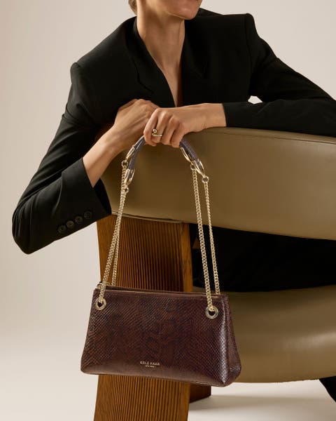 Woman holding a brown Cole Haan shoulder bag.