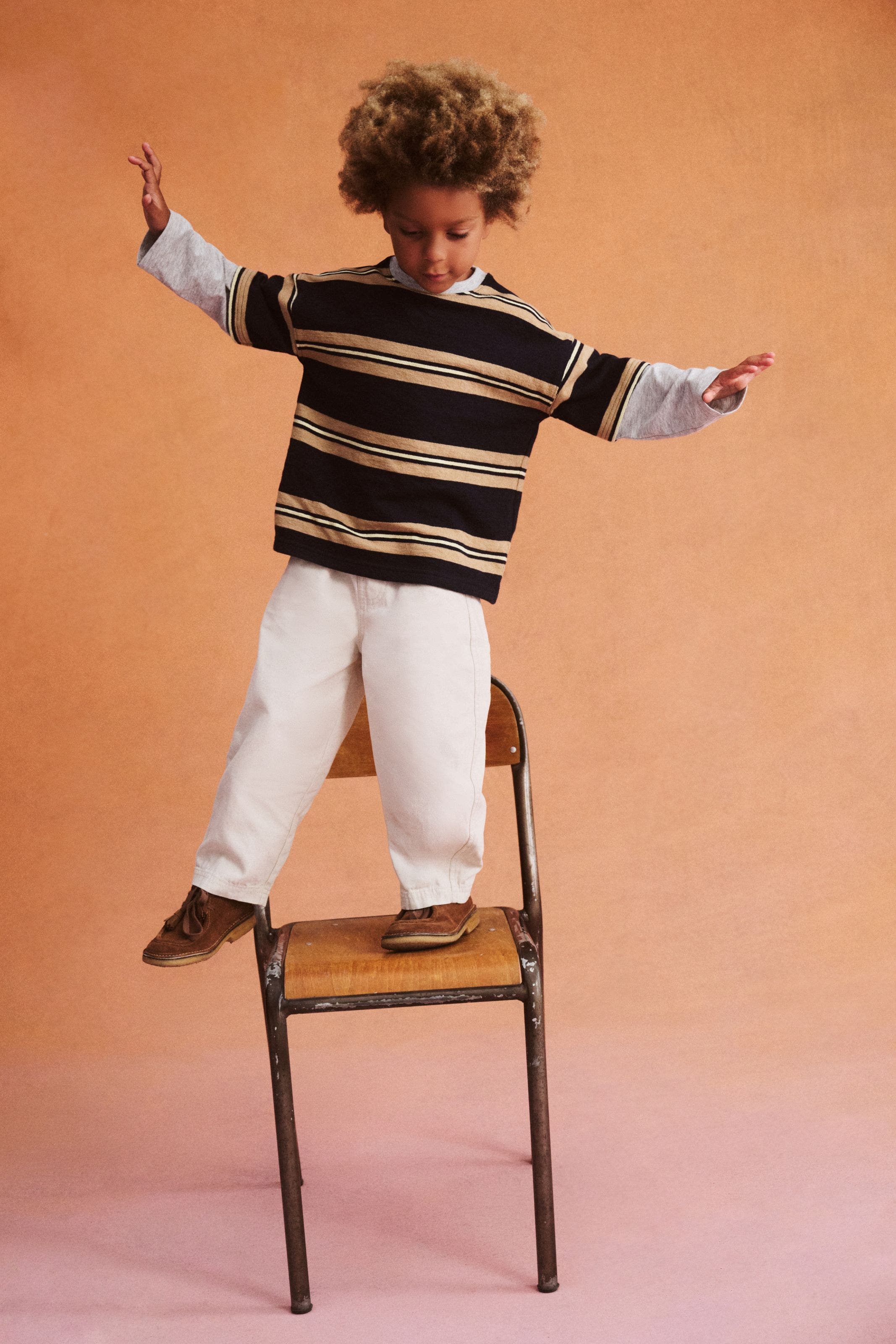 a boy in a stripe shirt standing on a chair