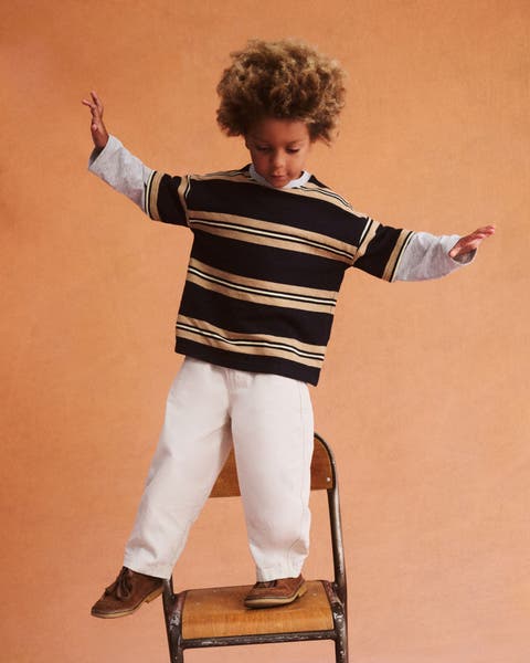 a boy in a stripe shirt standing on a chair