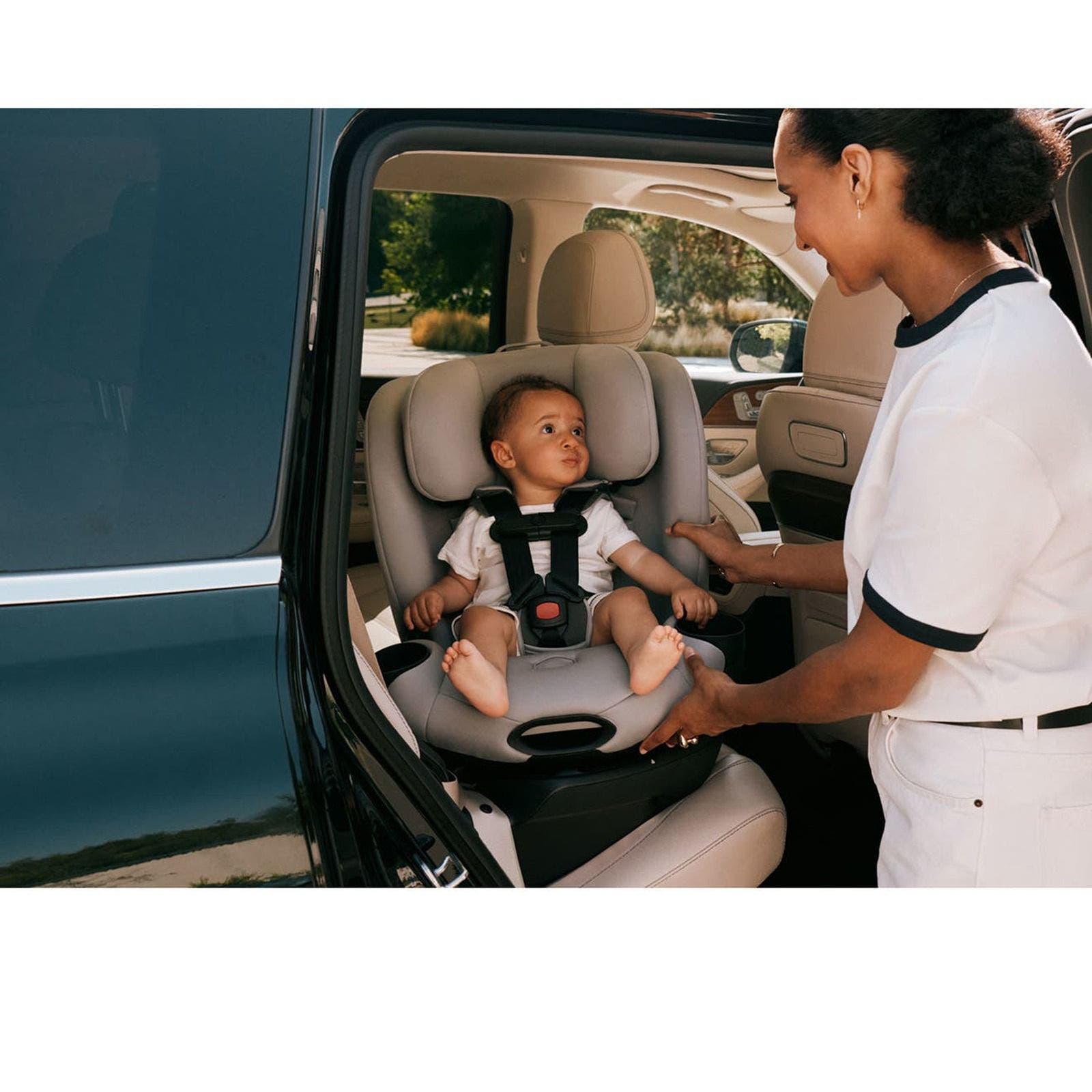 A woman buckling a baby into a gray CYBEX car seat in the back of an SUV.