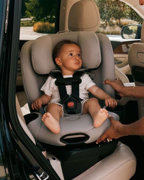 A woman buckling a baby into a gray CYBEX car seat in the back of an SUV.