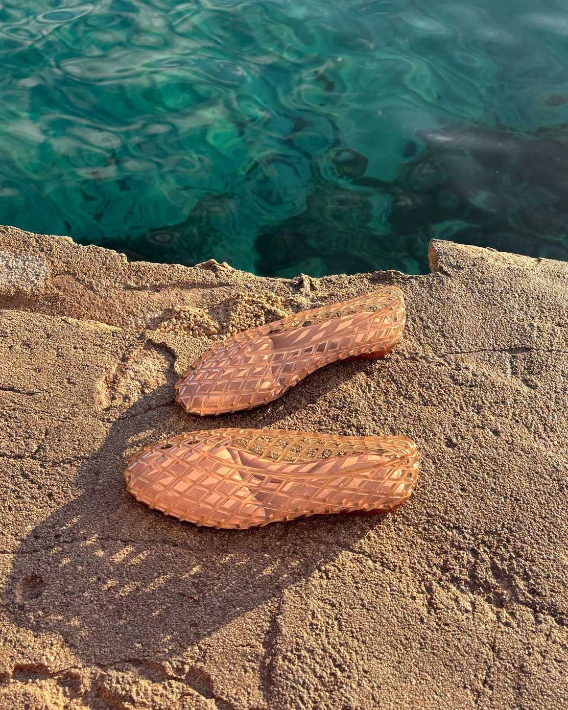 The Dolce Vita Jam jelly flat in Mocha Vinyl. A woman wearing a Dolce Vita jelly flat with fringed swim bottoms and a white tank.