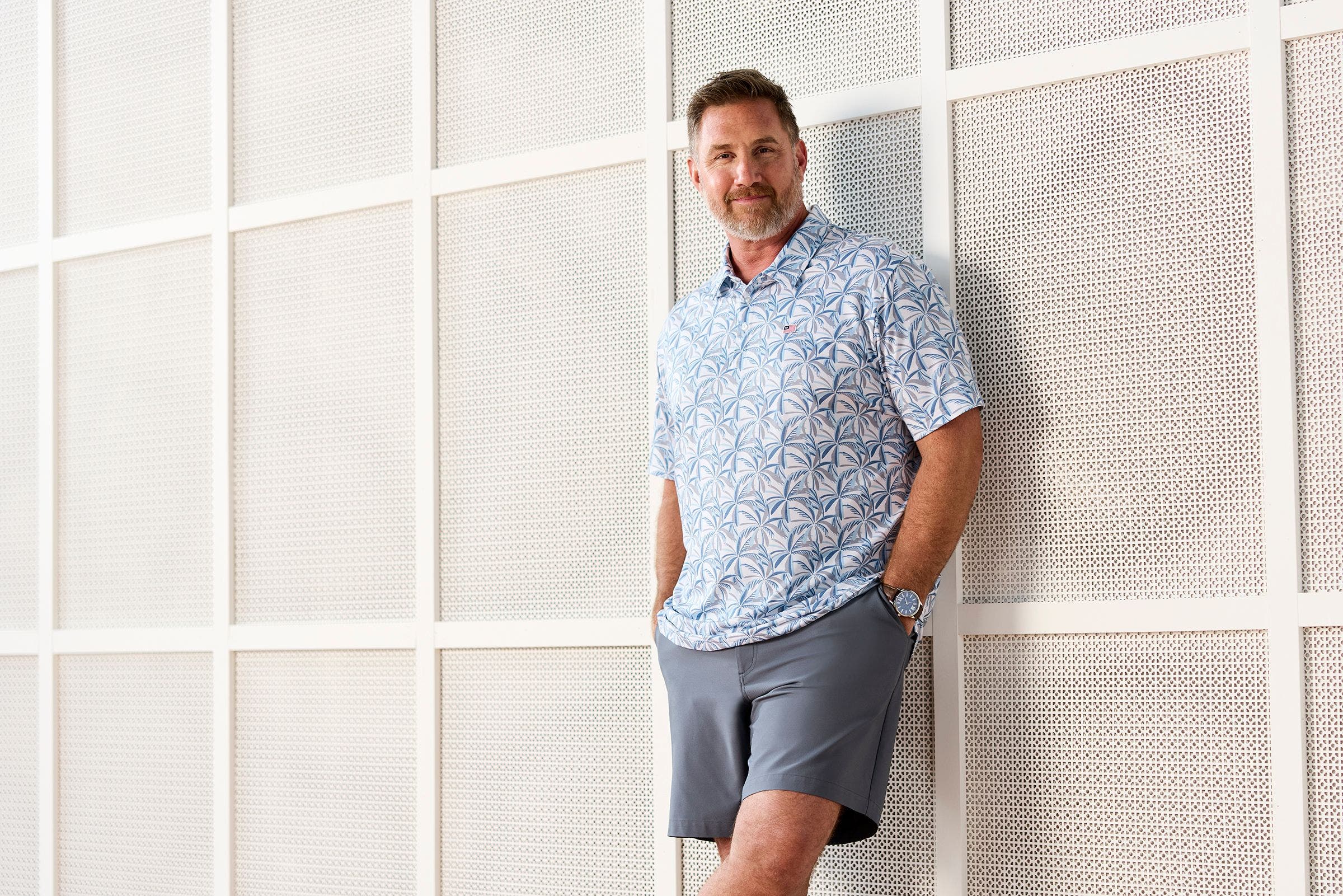 Man wearing floral print polo and grey shorts.
