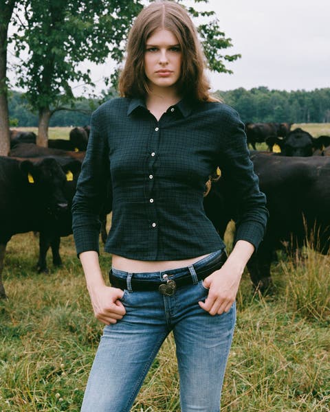 A woman wearing a button up shirt and low-rise jeans.