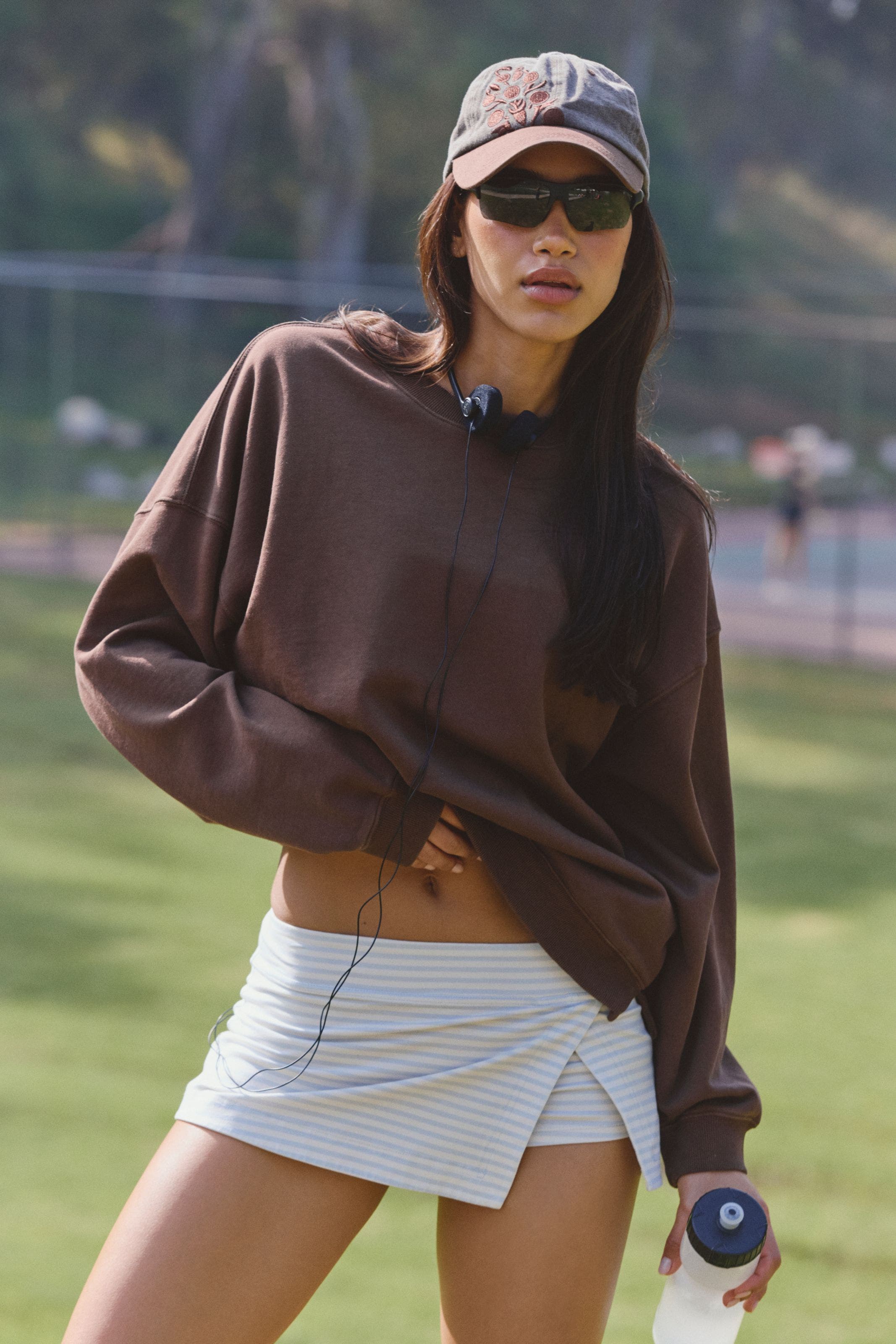 A woman wearing a brown active sweatshirt and a grey active mini skort.