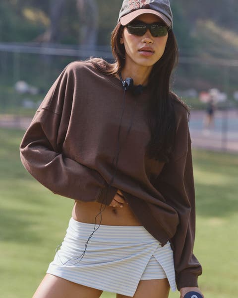 A woman wearing a brown active sweatshirt and a grey active mini skort.