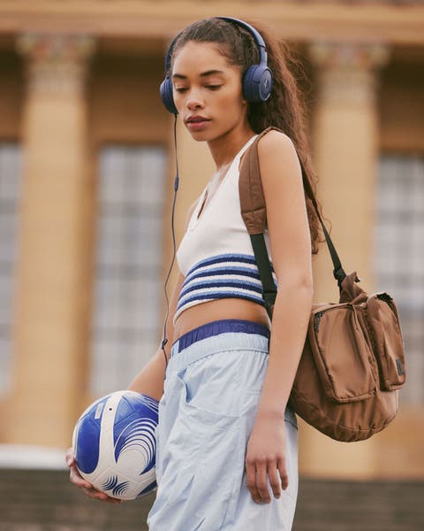 A woman with a soccer ball wearing a cropped tank and track pants.