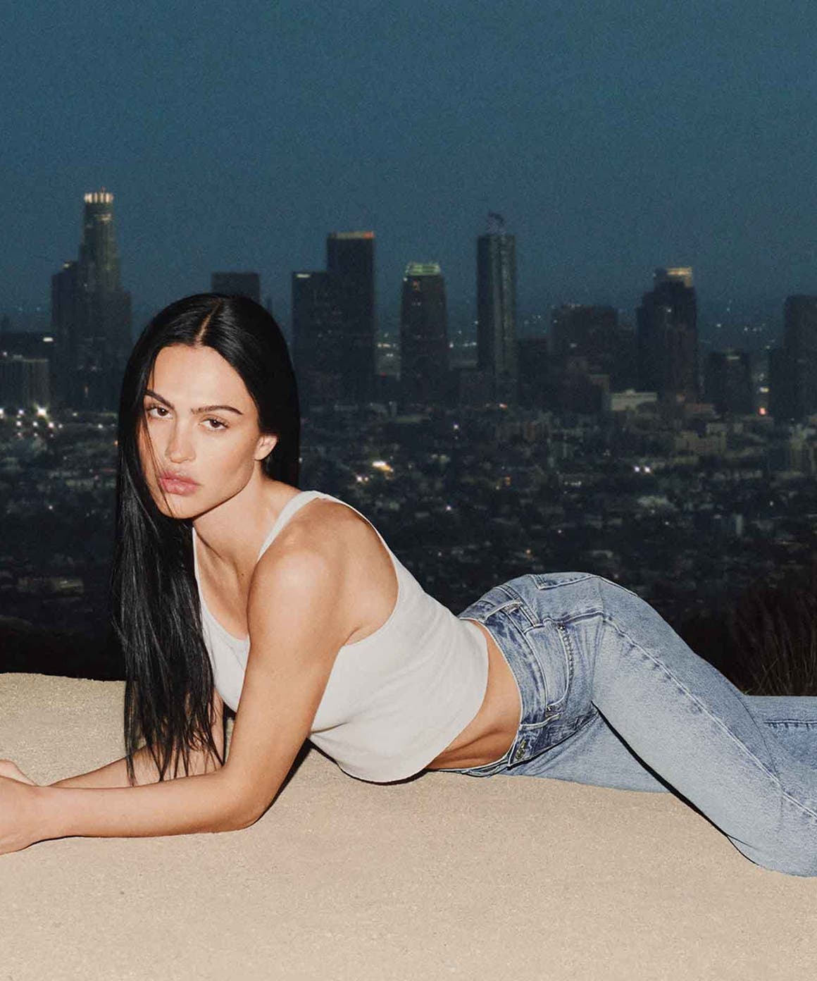 Woman wearing FRAME denim laying on sand.