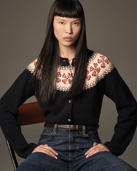 Woman sitting in a chair, wearing a cardigan and jeans with belt