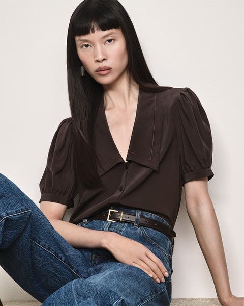 Woman sitting leaning, wearing dark brown blouse with puffy short sleeves