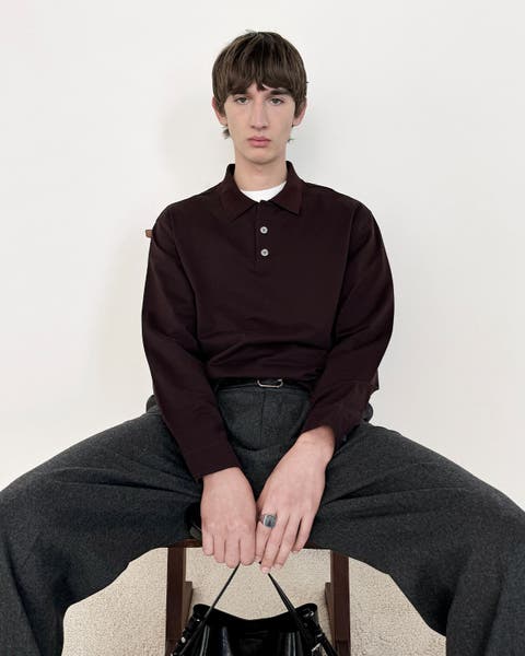 Man sitting in chair wearing collared long sleeve top and dark grey trousers