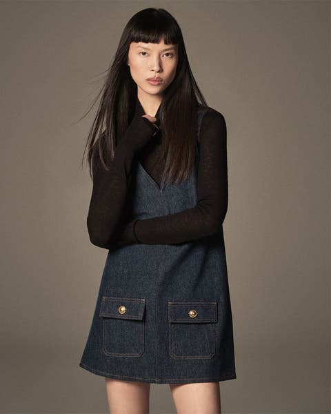 Woman standing wearing a denim dress with black long sleeve shirt under