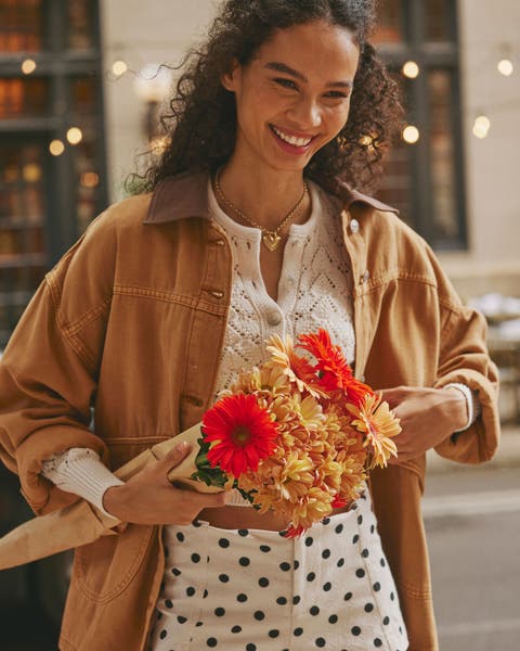 A woman wearing a utility jacket with a cardigan and shorts.