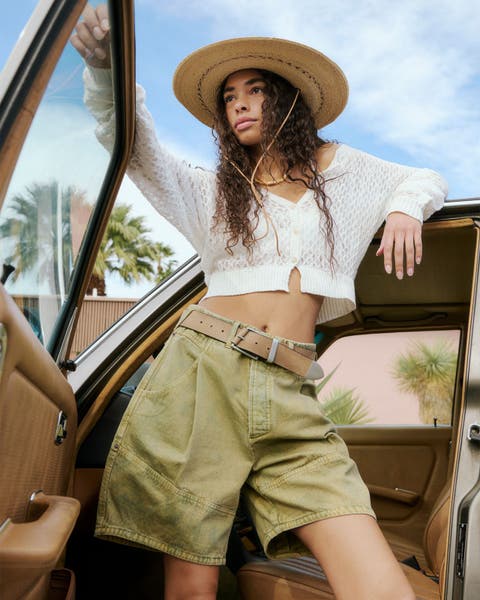 Woman wearing green cargo shorts and a white long sleeve top.