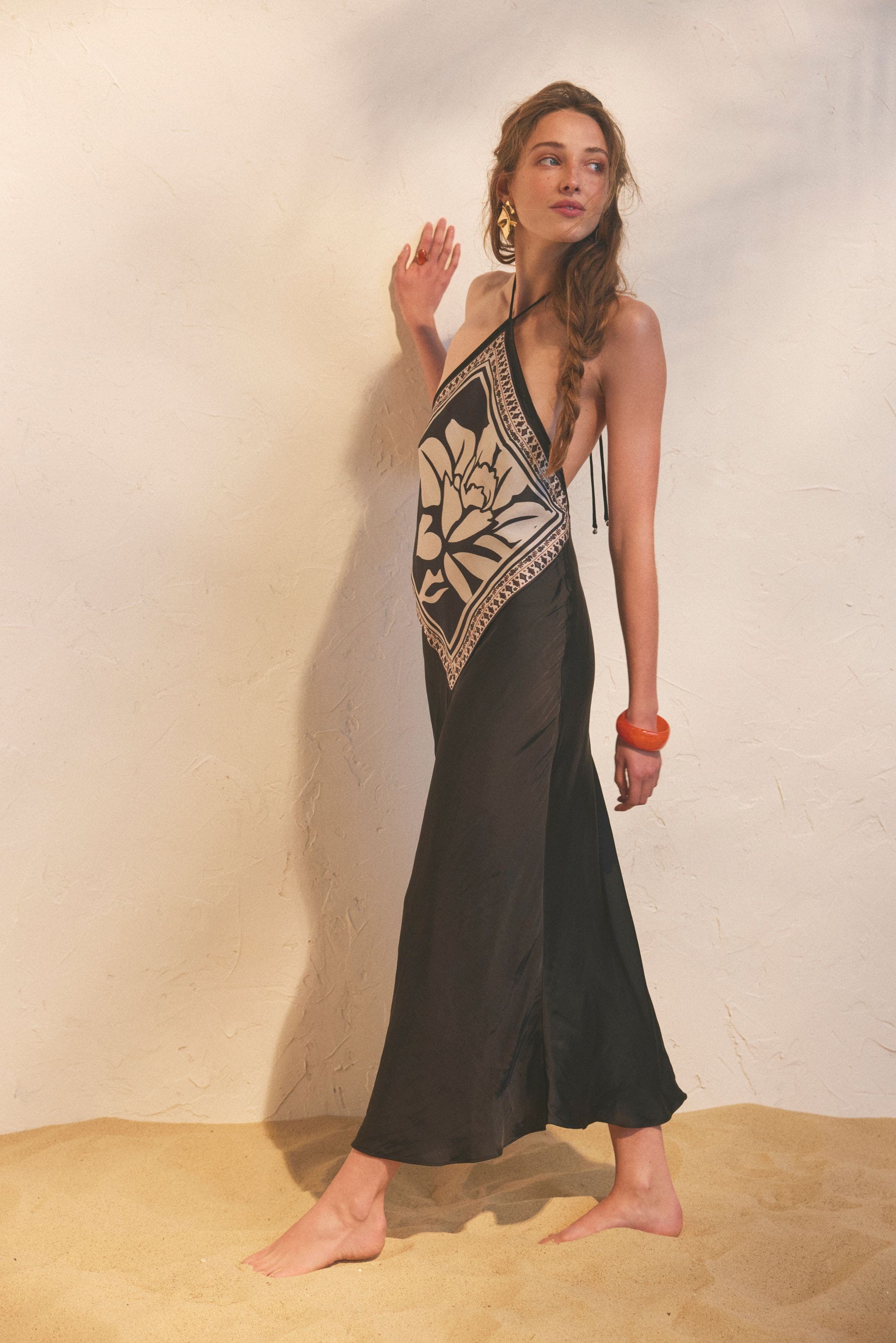 A woman wearing a black silky maxi dress with halter neck and white print. 