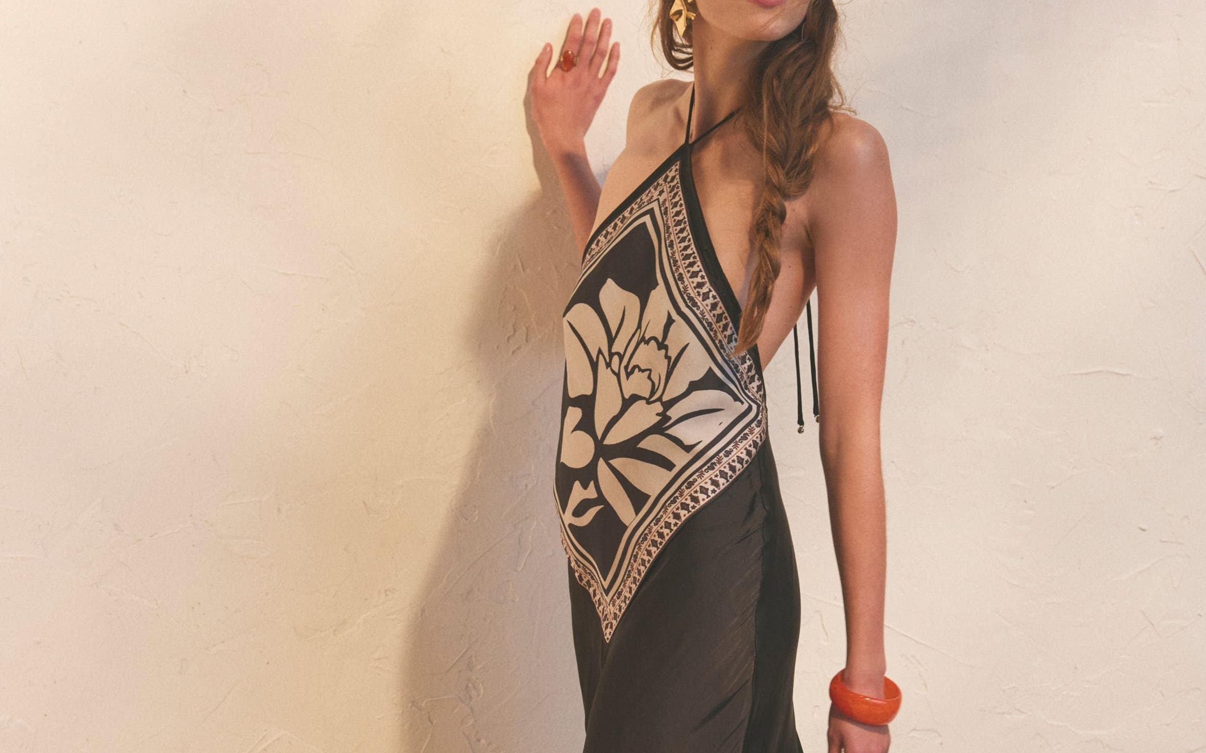 A woman wearing a black silky maxi dress with halter neck and white print.