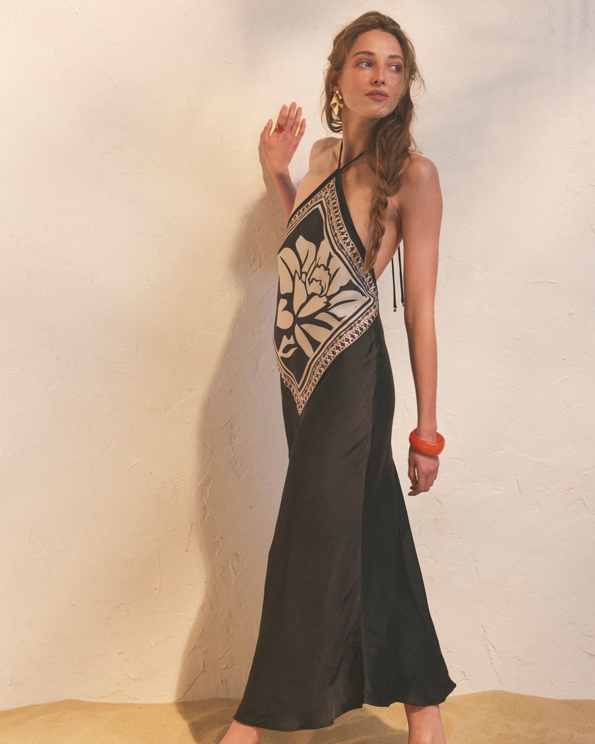 A woman wearing a black silky maxi dress with halter neck and white print.