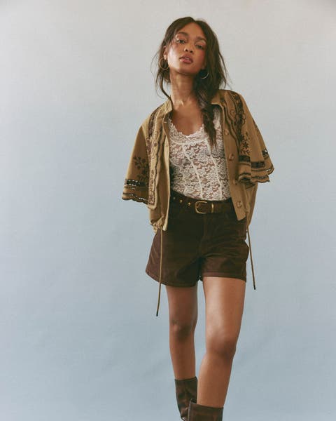 Woman wearing a lace top with light jacket, shorts with belt, and boots.