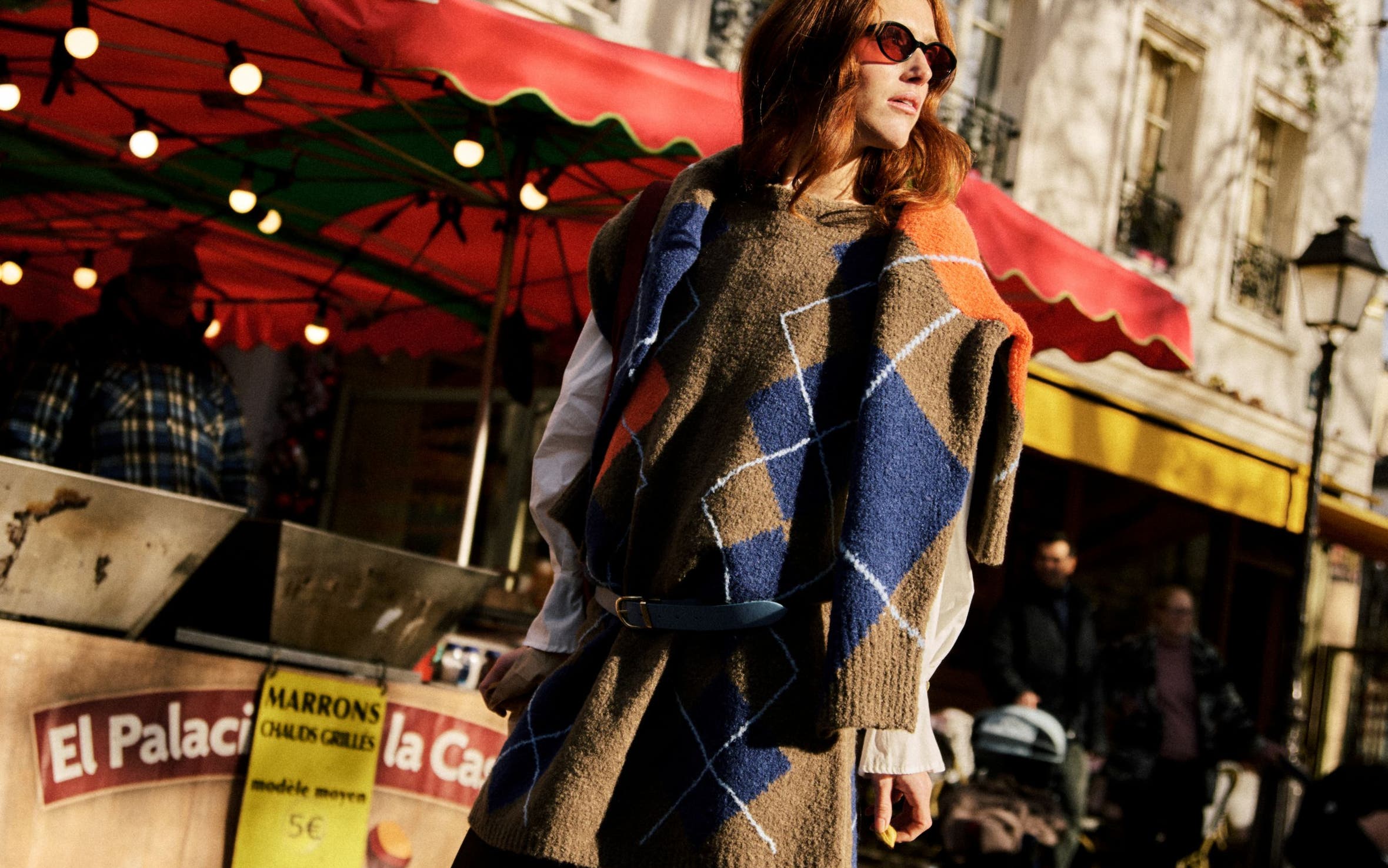 A woman wearing a patterned poncho and skirt in front of an outdoor market stall.