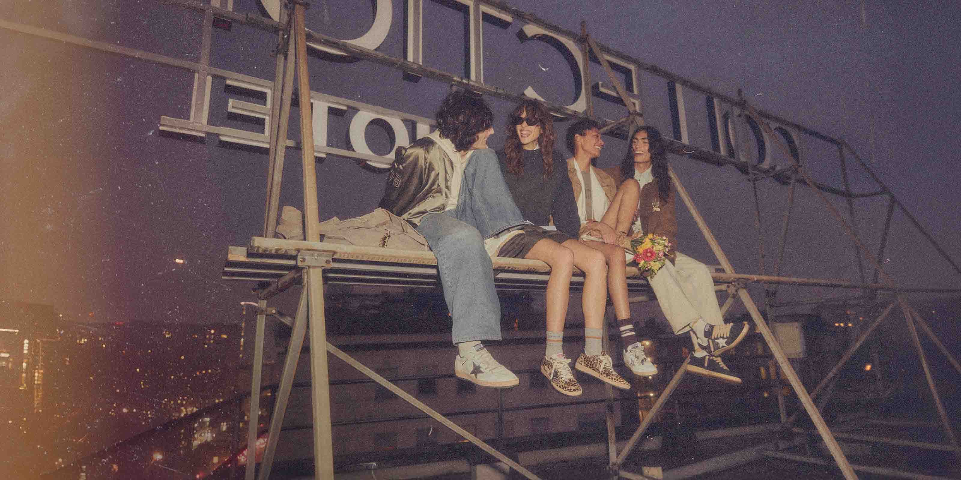 4 people sitting on a rooftop wearing Golden Goose shoes.