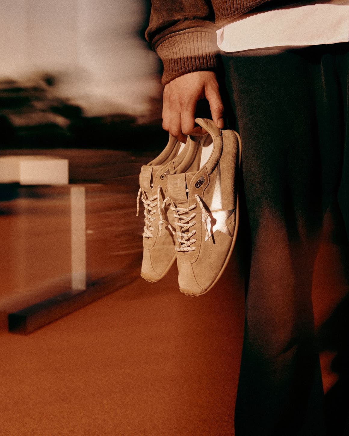 A man holding Golden Goose sneakers on a running track.