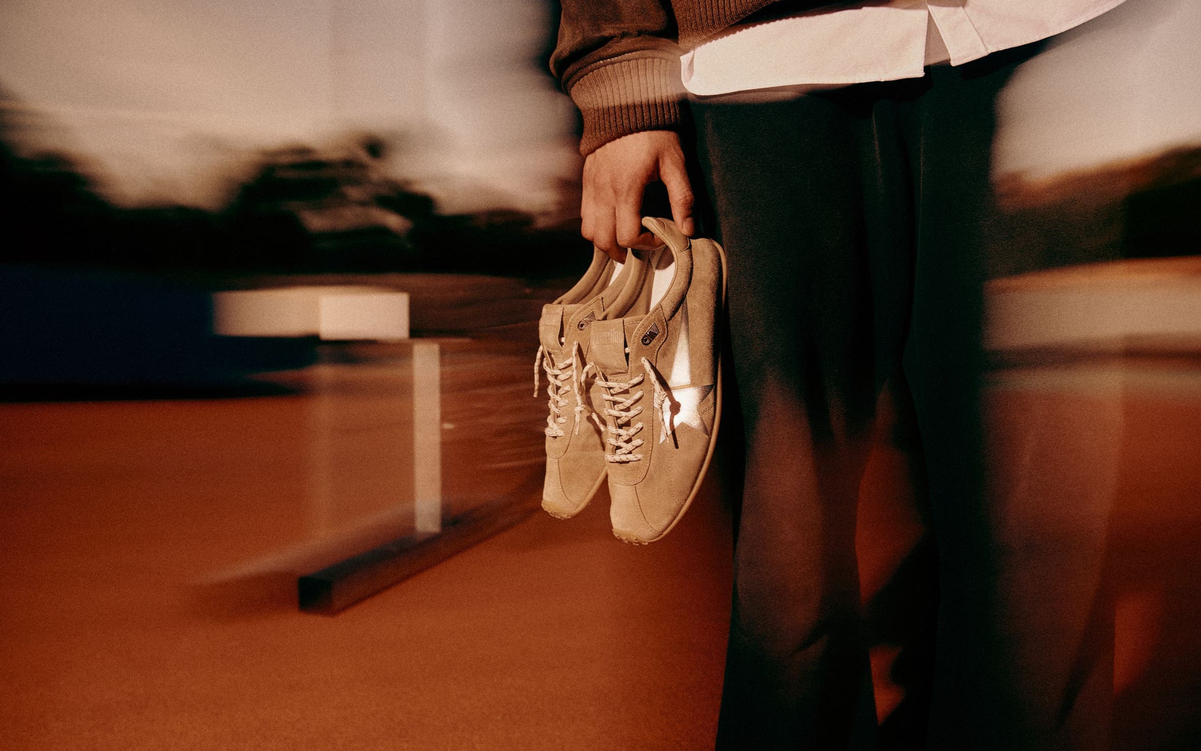 A man holding Golden Goose sneakers on a running track.