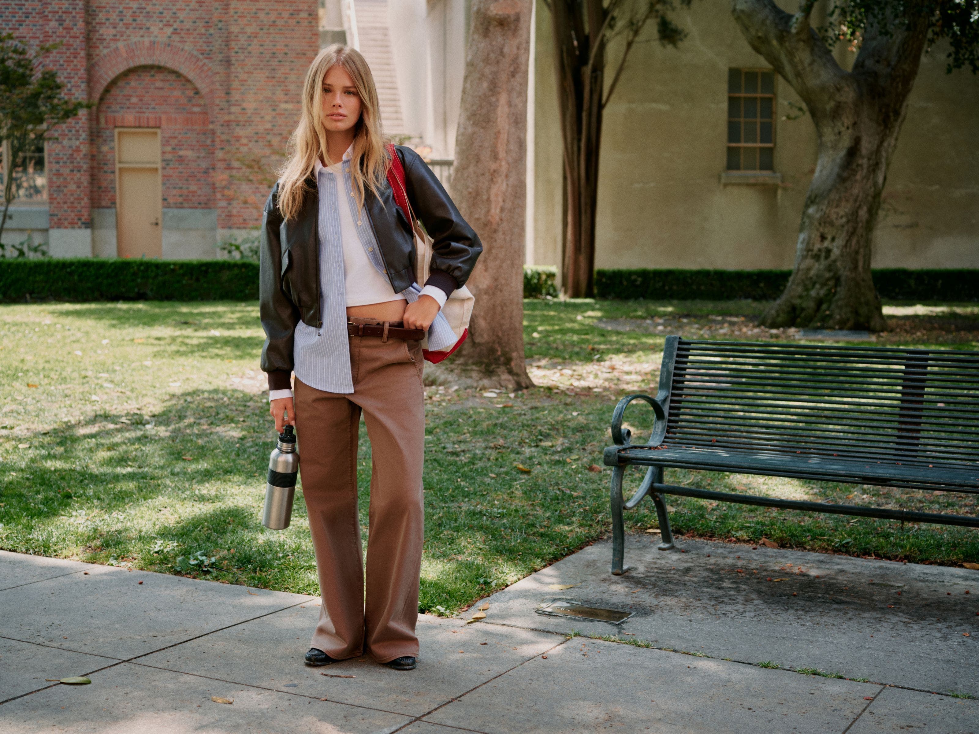 A woman wearing brown jeans, a white t-shirt, a blue Oxford shirt, ad a leather bomber.