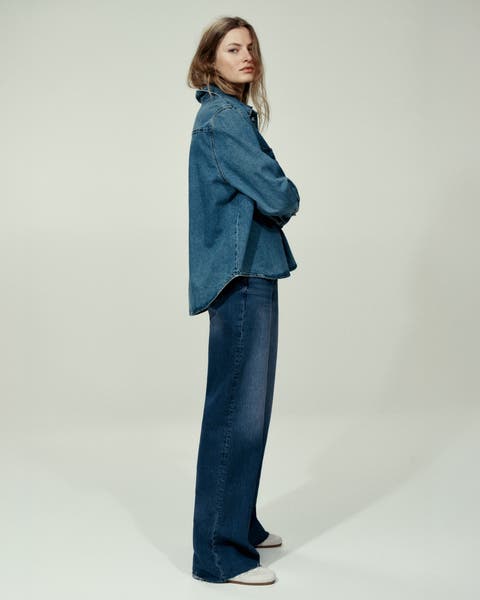 A woman wearing a denim button up and a pair of jeans.