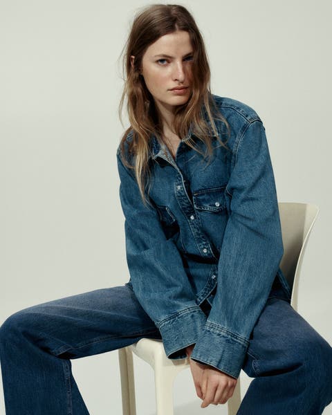 A woman wearing a denim shirt and jeans.