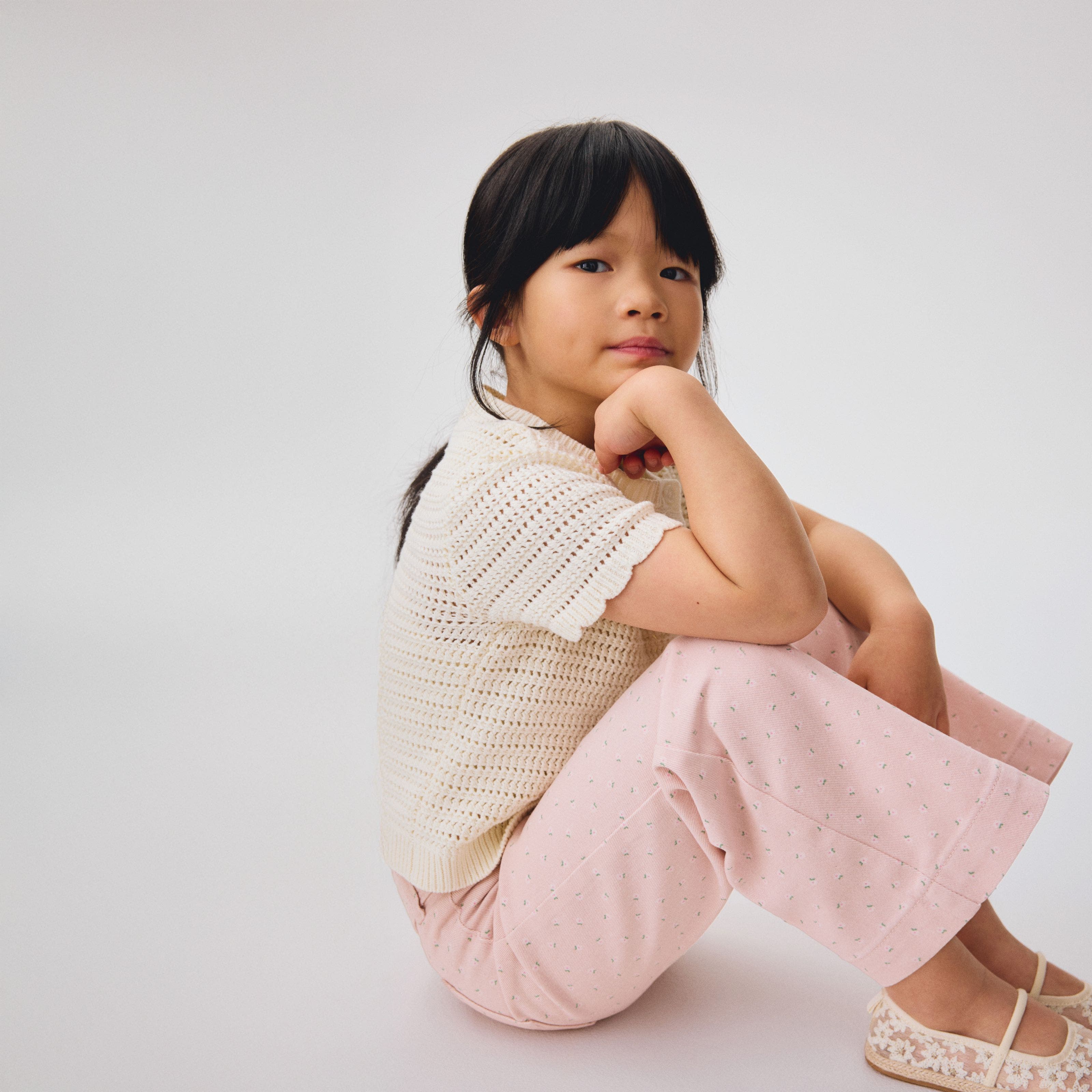 A girl wearing a knit top with pink floral-print pants and lace flats.