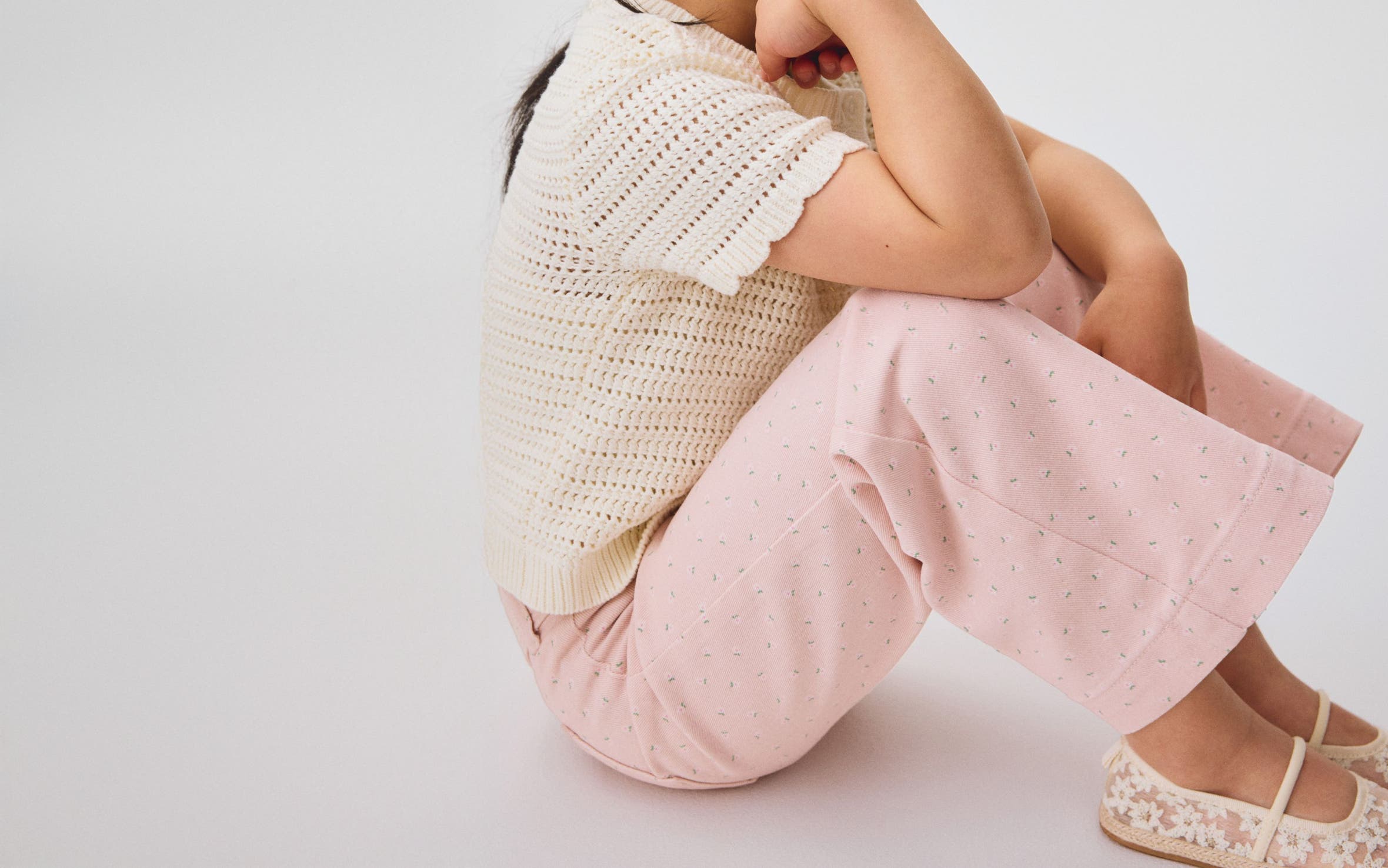 A little girl wearing a cream colored cardigan and pink pants from H&M.