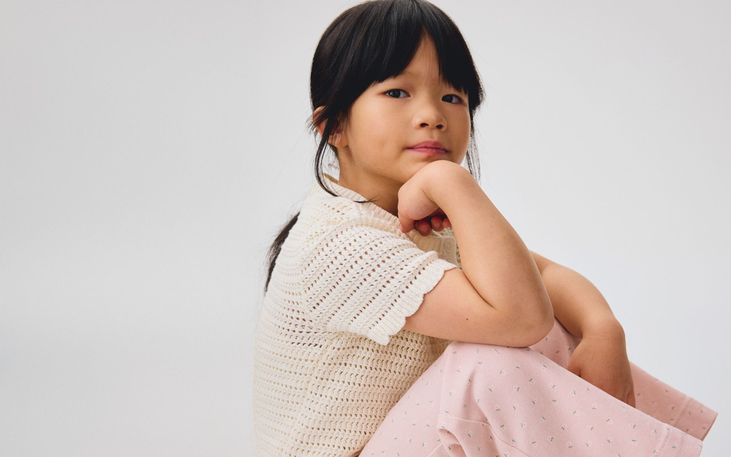 A girl wearing a cream scalloped cardigan and pink pants from H&M.