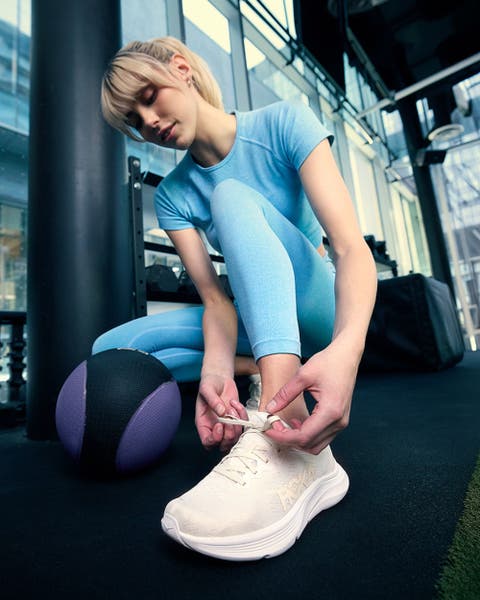 Woman tying the shoelace on a pair of white Hoka shoes.