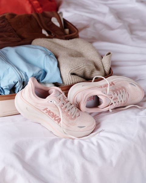 A pair of pink Hoka running shoes on a bed